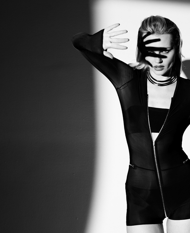 Model wearing Super-Sheer Feral Catsuit-Romper for a bold night-out look, featuring a 2-way zipper and thumb-hole sleeves, styled with necklace, Spotlight Ring Bandeau and Ubi Black Panty for a seductive, edgy outfit.